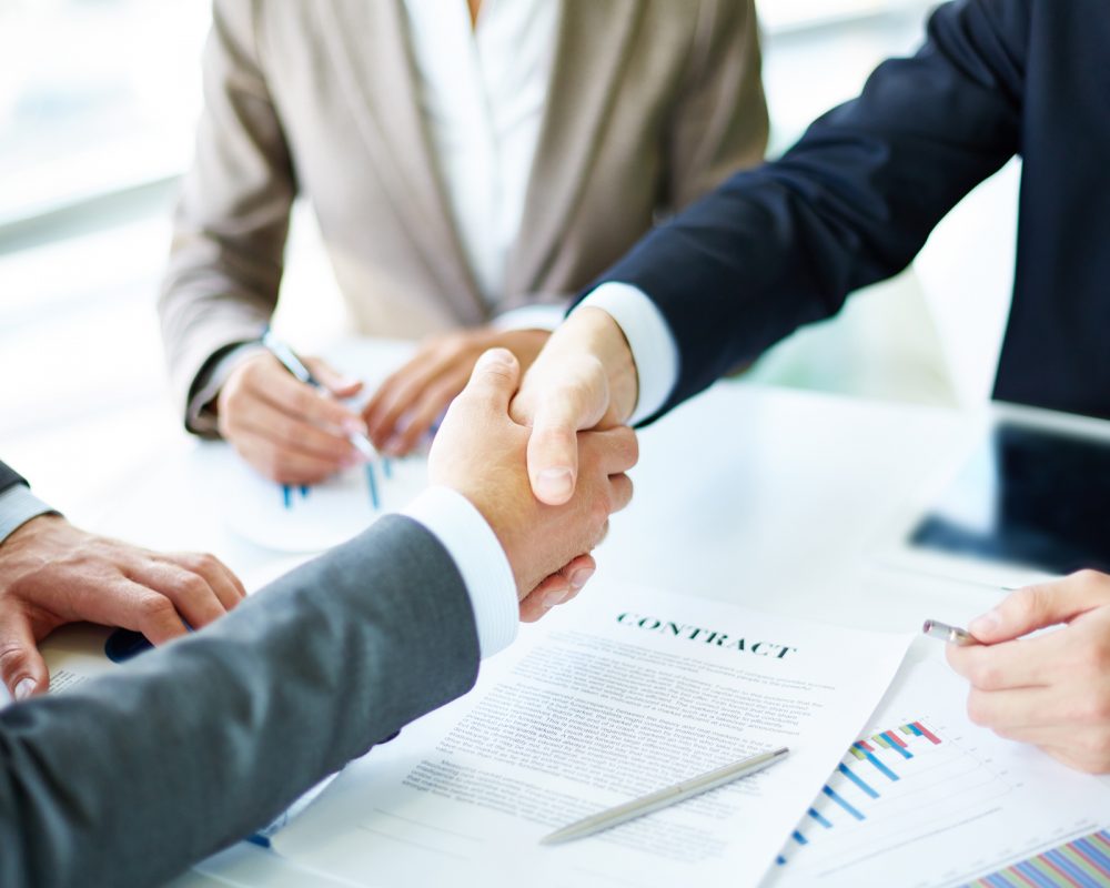 Image of business partners handshaking over business objects on workplace